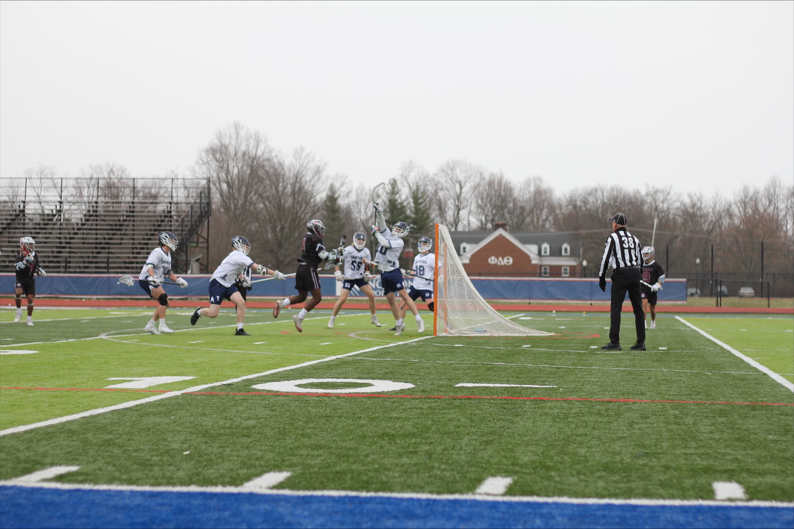 Collegiate lacrosse goalie leaping to deflect a shot near the goal